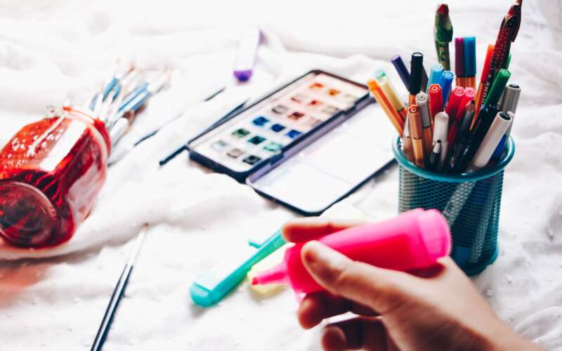 person holding pink highlighter with pens and paint brushes in the background