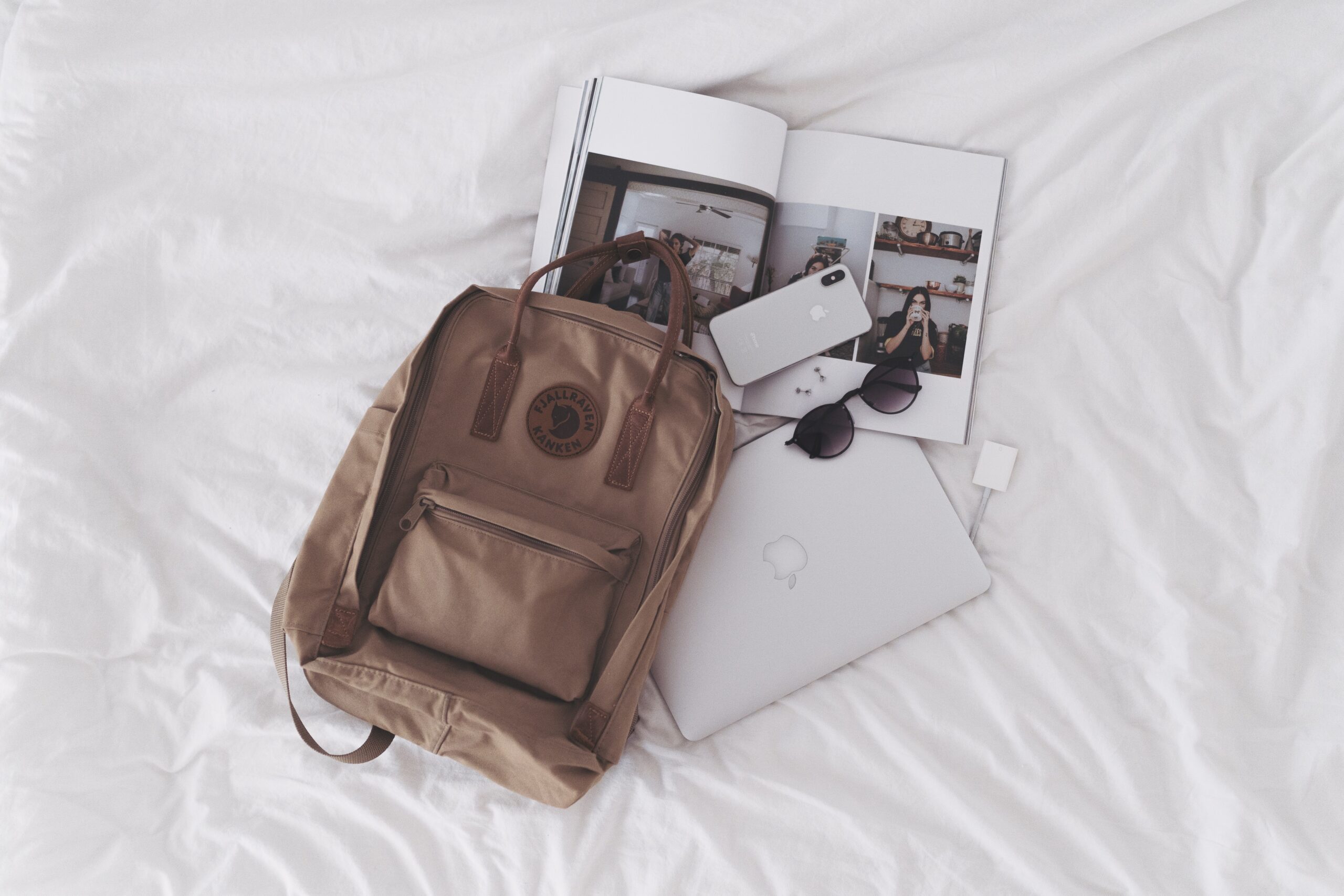 backpack and laptop laying on white bed