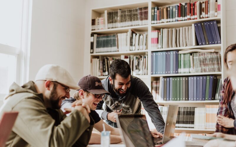 Three men laughing while looking at laptop in library