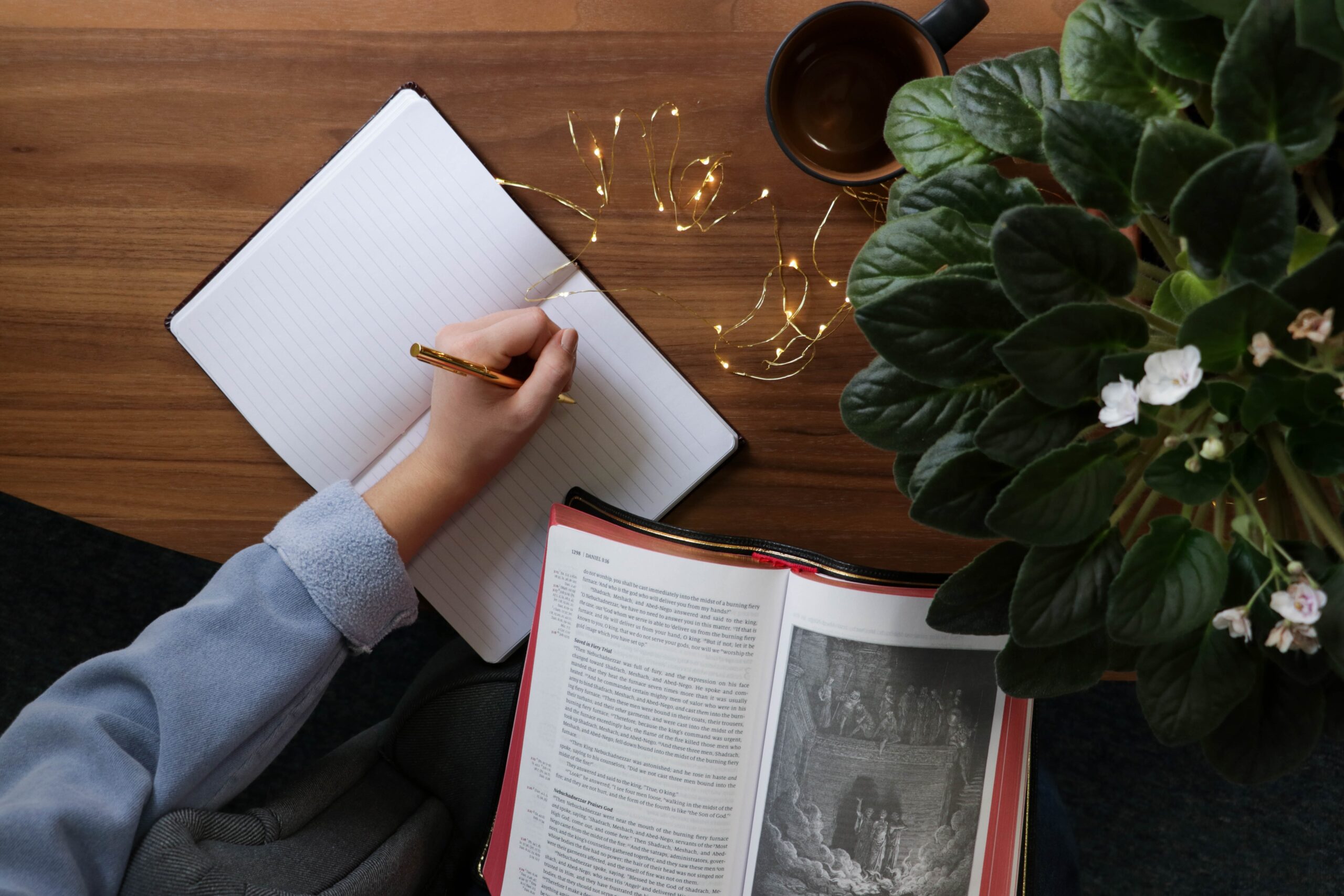 man sitting at a table while writing in a notebook and reading a book - procrastination in college. Empty white spiral book