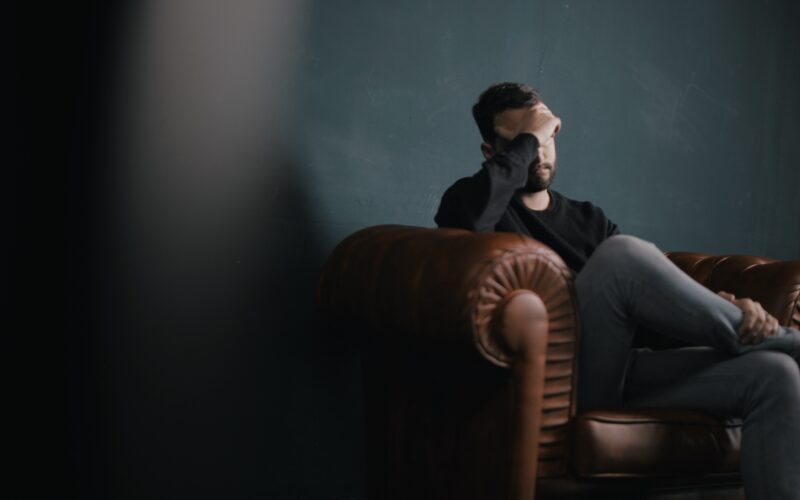 Man sitting on couch with his hand on his head