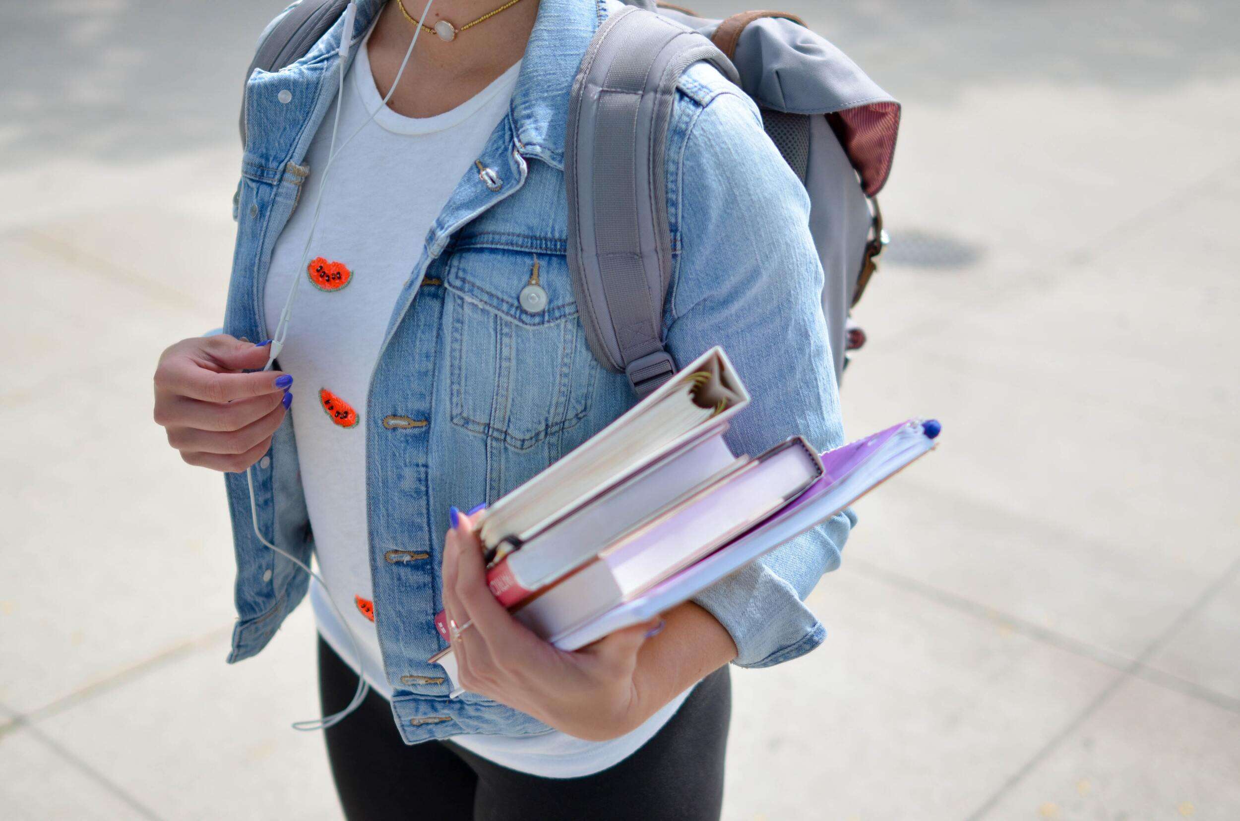 college student wearing denim jacket holding books and folders