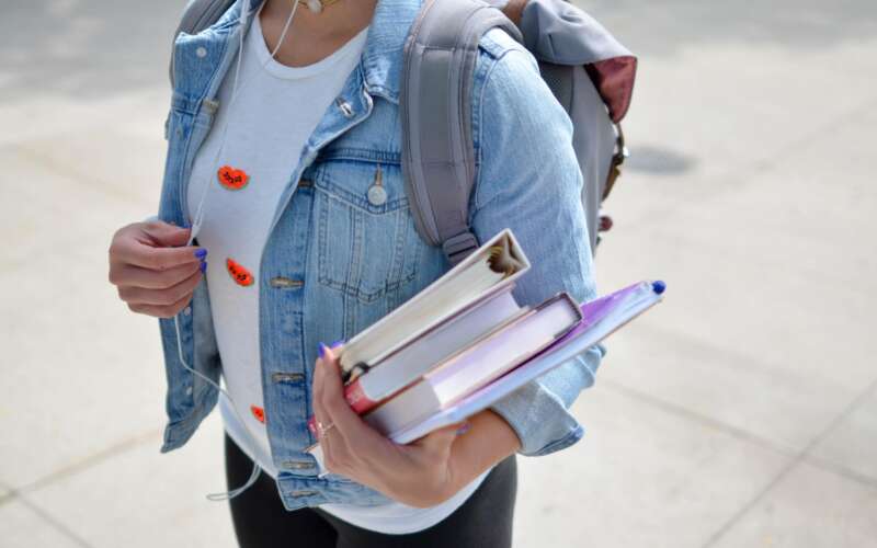 college student wearing denim jacket holding books and folders