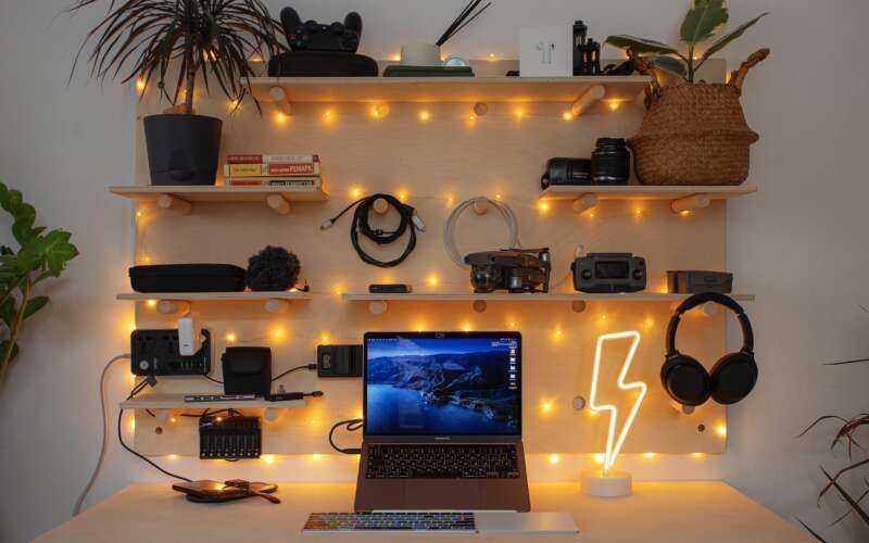 laptop on desk with shelving and warm lights on the wall behind it