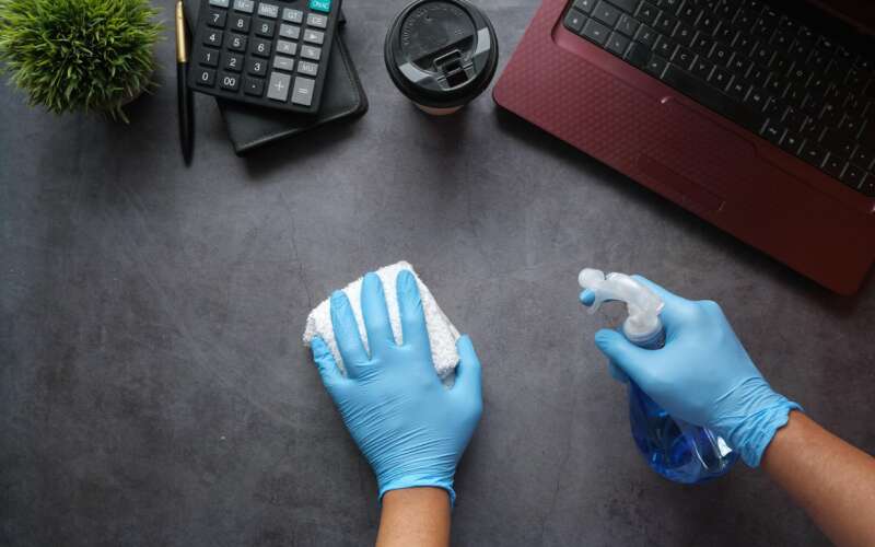 Person cleaning table with laptop on it while wearing blue latex gloves