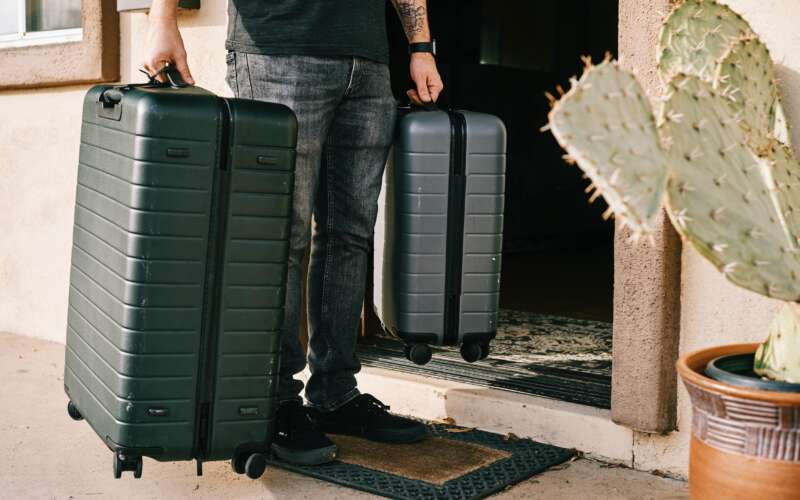man in back jeans holding two grey suitcases