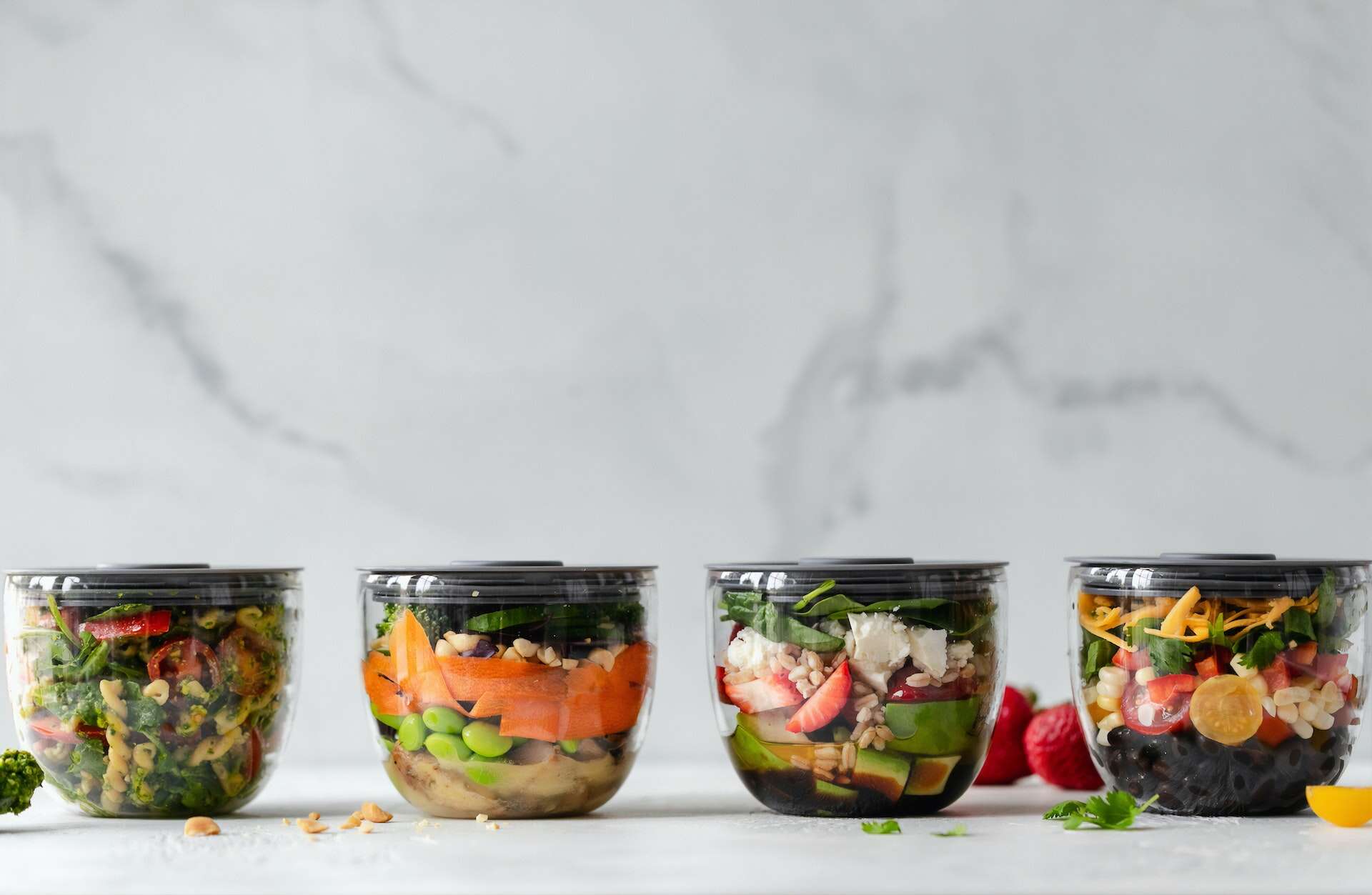 Four small clear food storage containers with fruit and vegetables in them