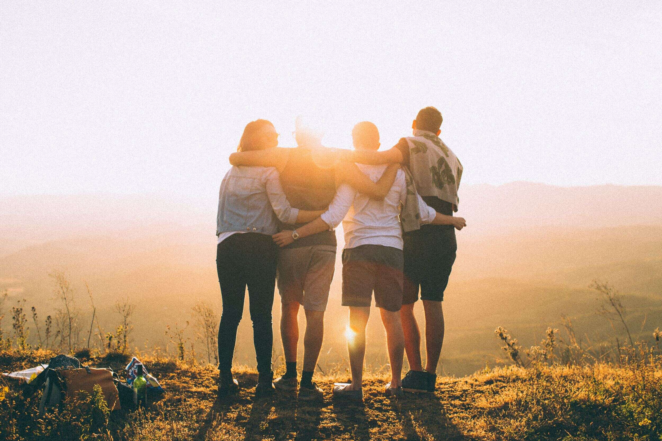 four friends hugging while watching the sunset outdoors