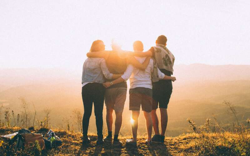 four friends hugging while watching the sunset outdoors