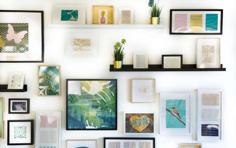 assortment of colorful framed paintings and plants on a white wall