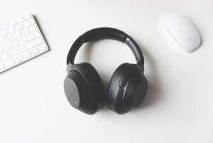 black wireless headphones laying on a white table between white Apple mouse and keyboard