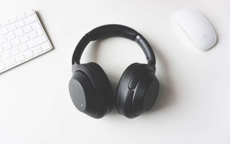 black wireless headphones laying on a white table between white Apple mouse and keyboard