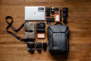Dark grey backpack, laptop, and other backpack essentials laying wood floor