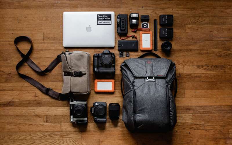 Dark grey backpack, laptop, and other backpack essentials laying wood floor
