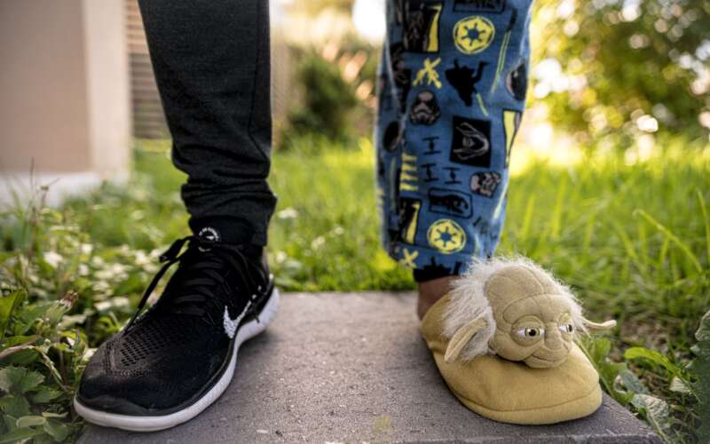 Person outside wearing a black Nike sneaker on one foot and a Star Wars Yoda slipper on the other foot