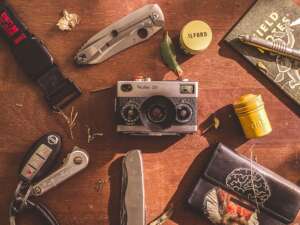 camera, watch, folding knife, and other edc items on wooden table