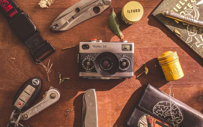 camera, watch, folding knife, and other edc items on wooden table