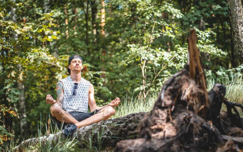 Man sitting on a log meditating in the woods