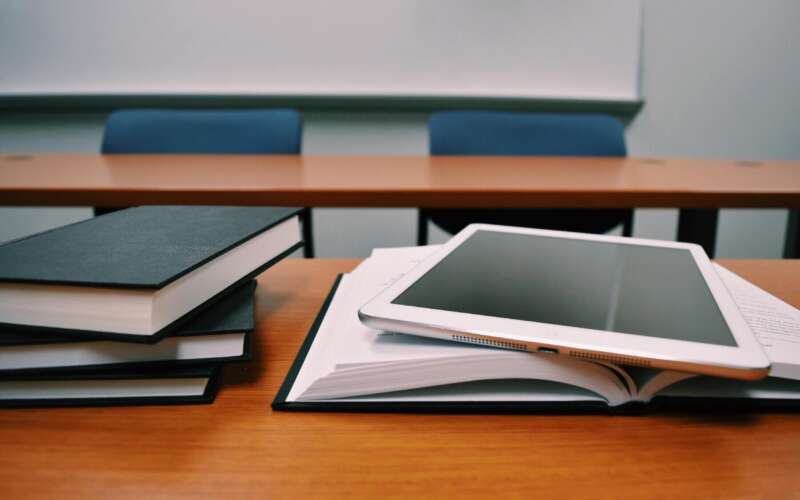 Books and a tablet laying on a desk in a classroom