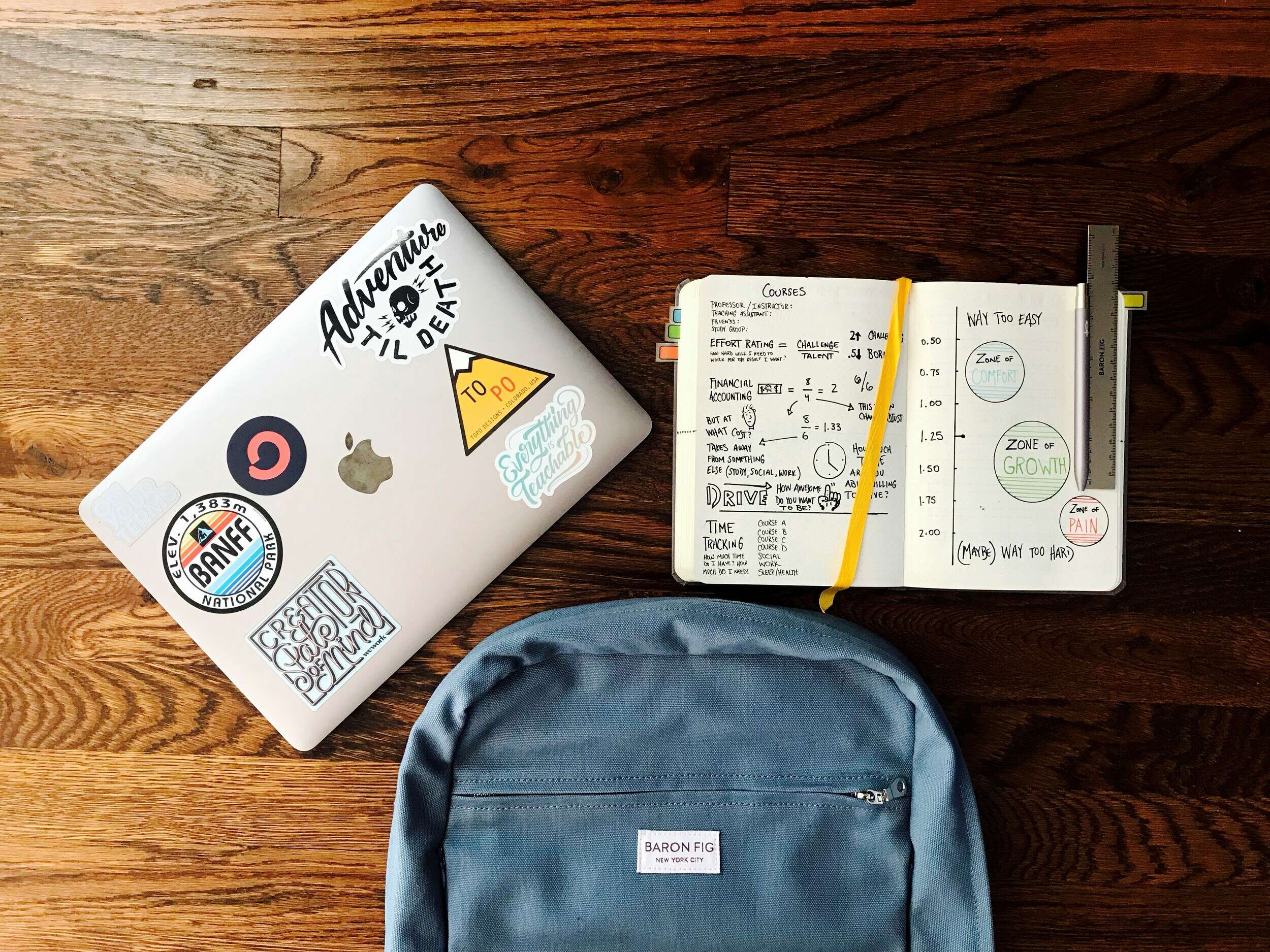 Laptop, backpack, and an open notebook laying on a wood table.