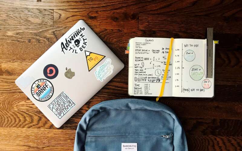Laptop, backpack, and an open notebook laying on a wood table.