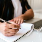 Mastering the Art of Note-Taking in College Person writing in a notebook and on their laptop