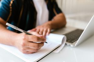 Person writing in a notebook and on their laptop