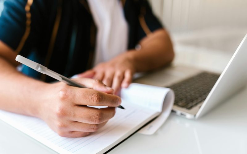 Person writing in a notebook and on their laptop