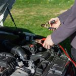 Man in gray shirt connect jumper cables to car battery