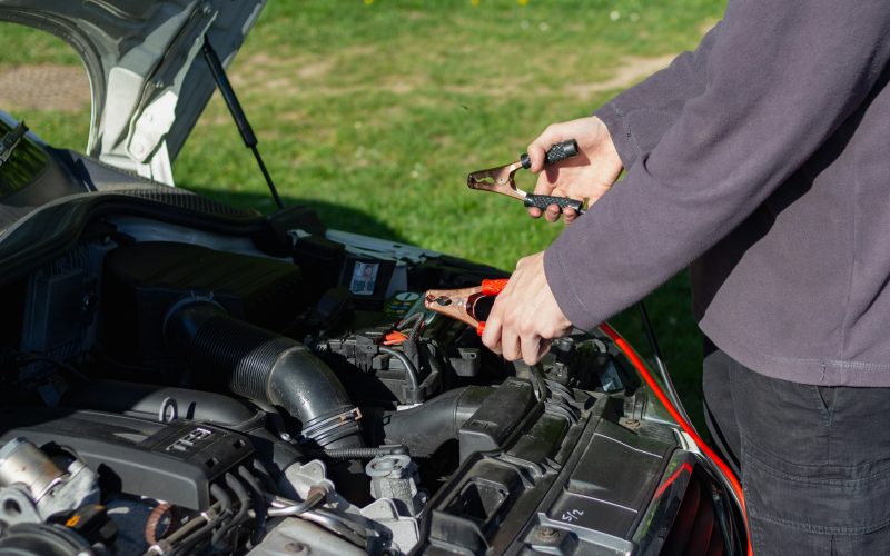 Man in gray shirt connect jumper cables to car battery