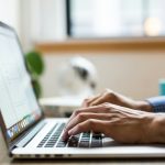 Person typing on a laptop beside a window during the day.