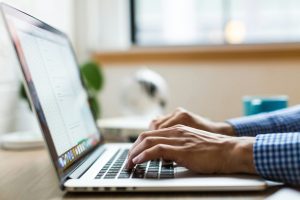 Person typing on a laptop beside a window during the day.