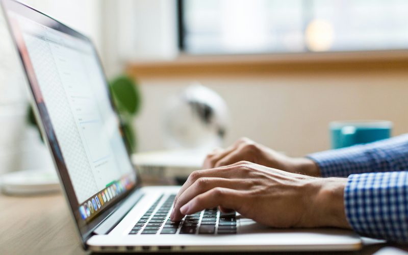 Person typing on a laptop beside a window during the day.