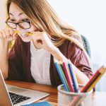 Women biting a pencil and looking stressed while sitting in front of a laptop during the day