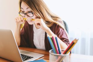 Women biting a pencil and looking stressed while sitting in front of a laptop during the day
