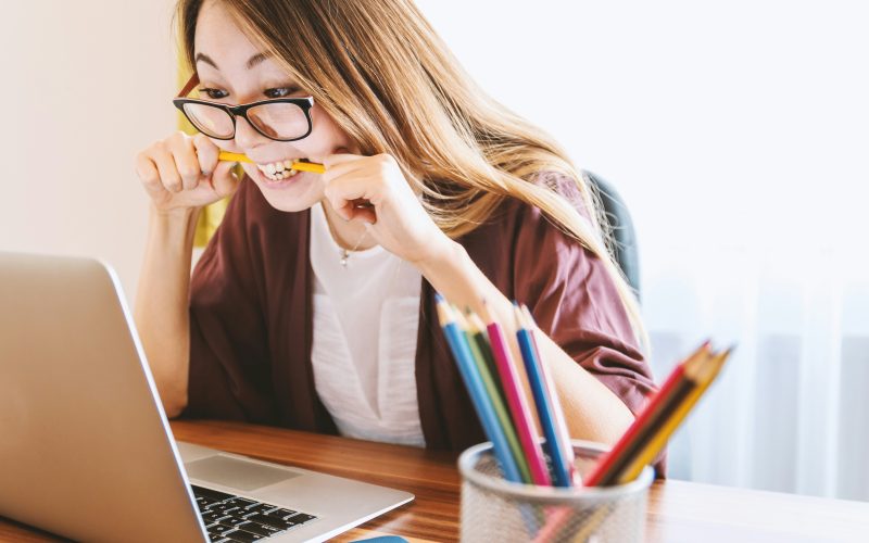 Women biting a pencil and looking stressed while sitting in front of a laptop during the day