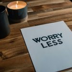 Candle and a white card on wood table that says worry less