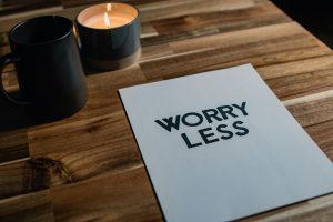 Candle and a white card on wood table that says worry less