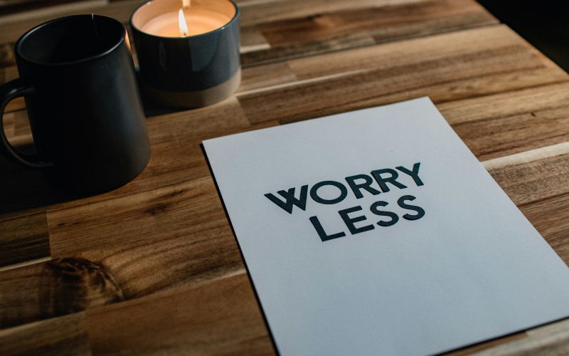 Candle and a white card on wood table that says worry less