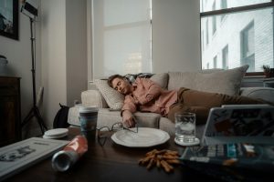 Man sleeping on couch during the day with trash on coffee table