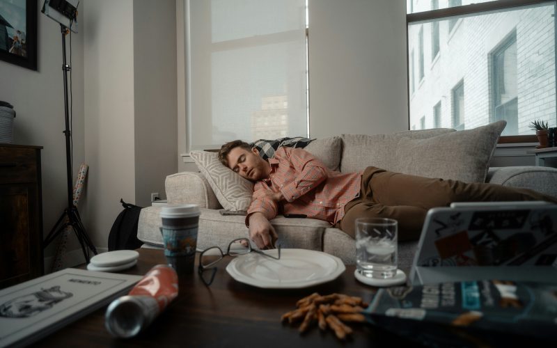 Man sleeping on couch during the day with trash on coffee table