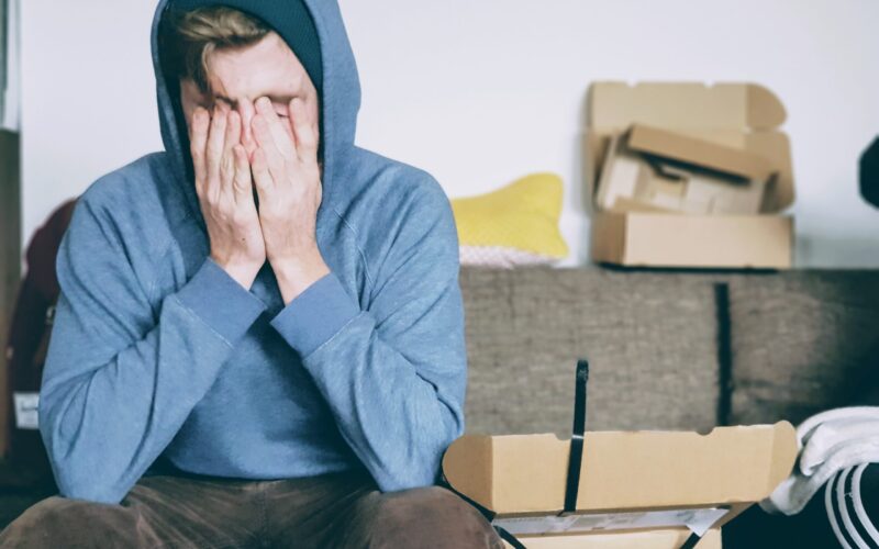 Guy in hoodie sitting down with his hands over his face